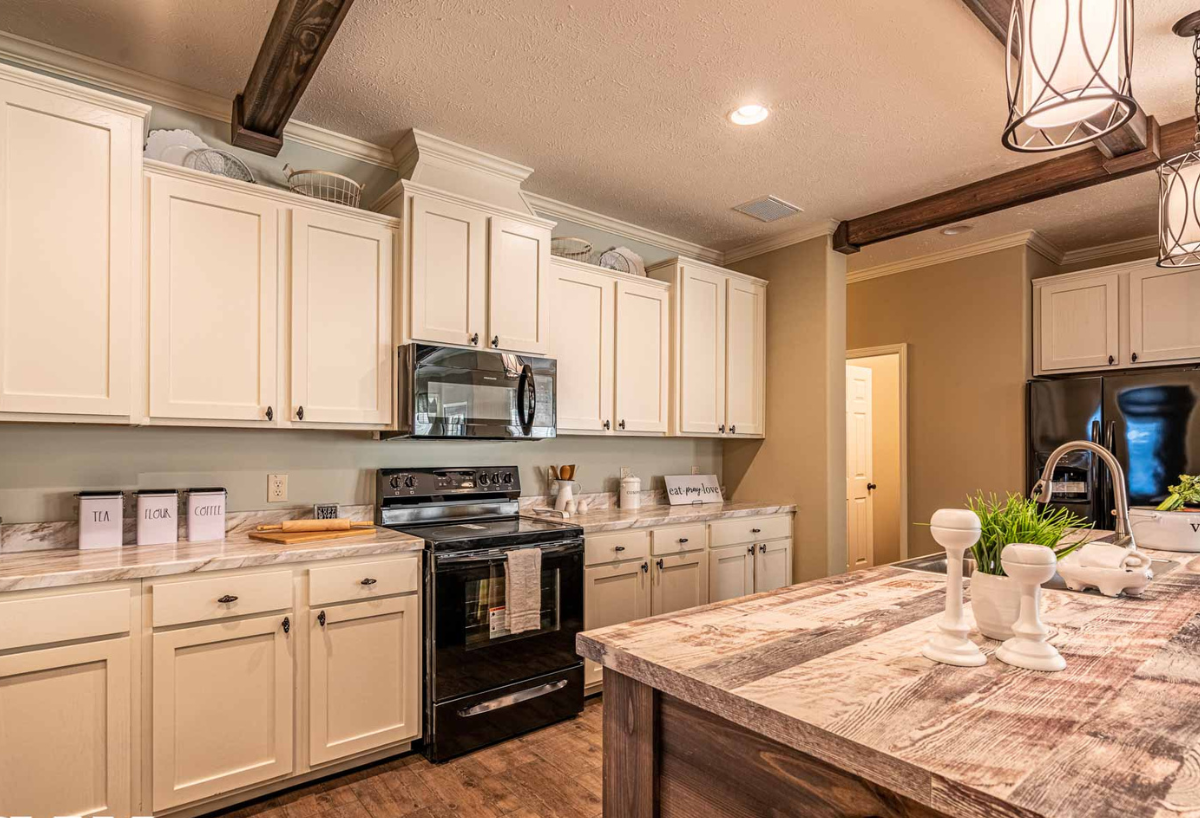 Warm, rustic kitchen with wooden beams, white cabinets, black appliances, and a center island. Soft lighting creates a cozy, inviting atmosphere.
