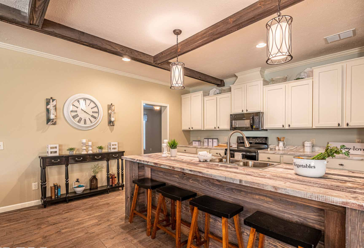 Spacious kitchen with rustic beams, white cabinets, and a large wooden island with four stools. Warm lighting and decor create a cozy atmosphere.