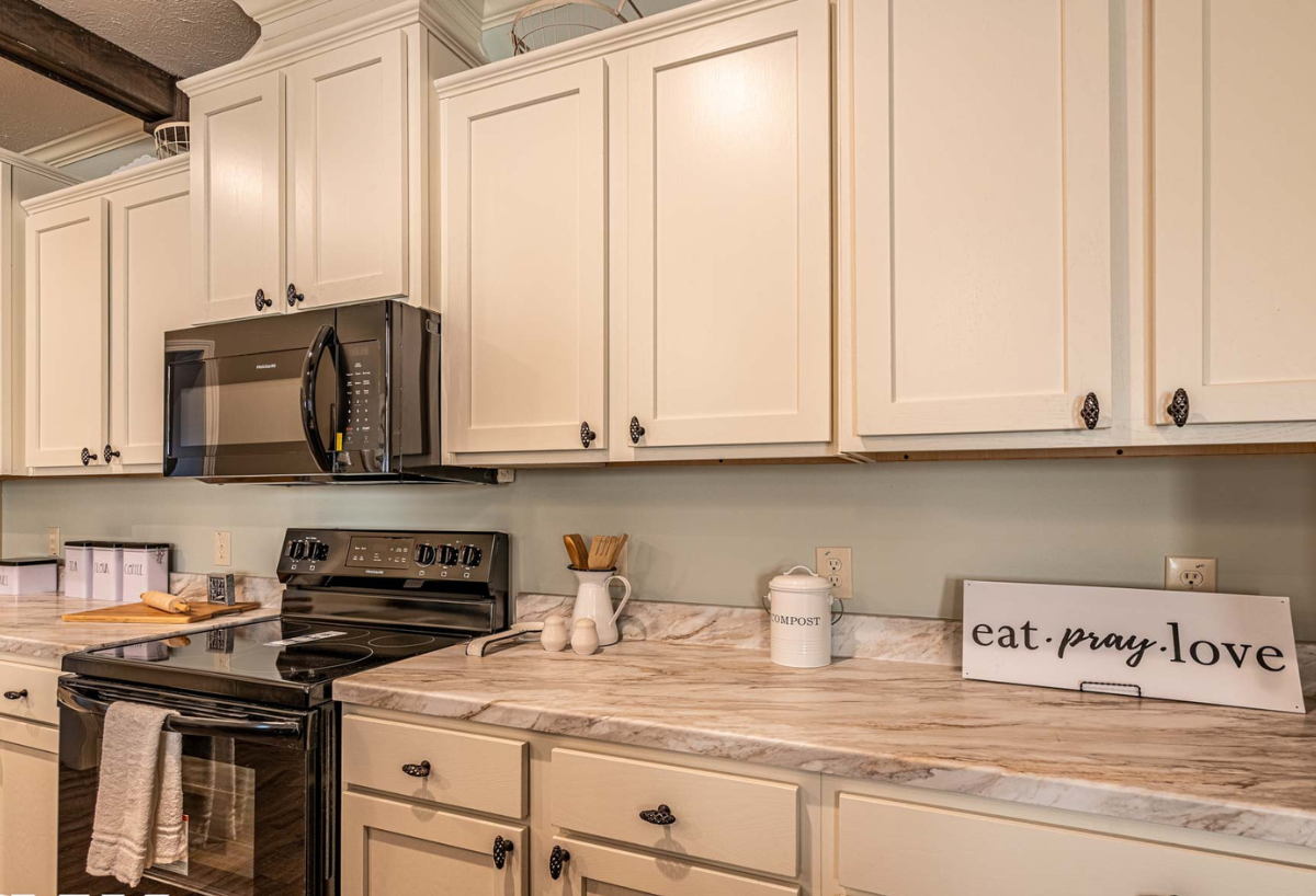Modern kitchen with white cabinets and grey countertops. A black stove and microwave are centered. A sign reads "eat. pray. love." creating a cozy vibe.