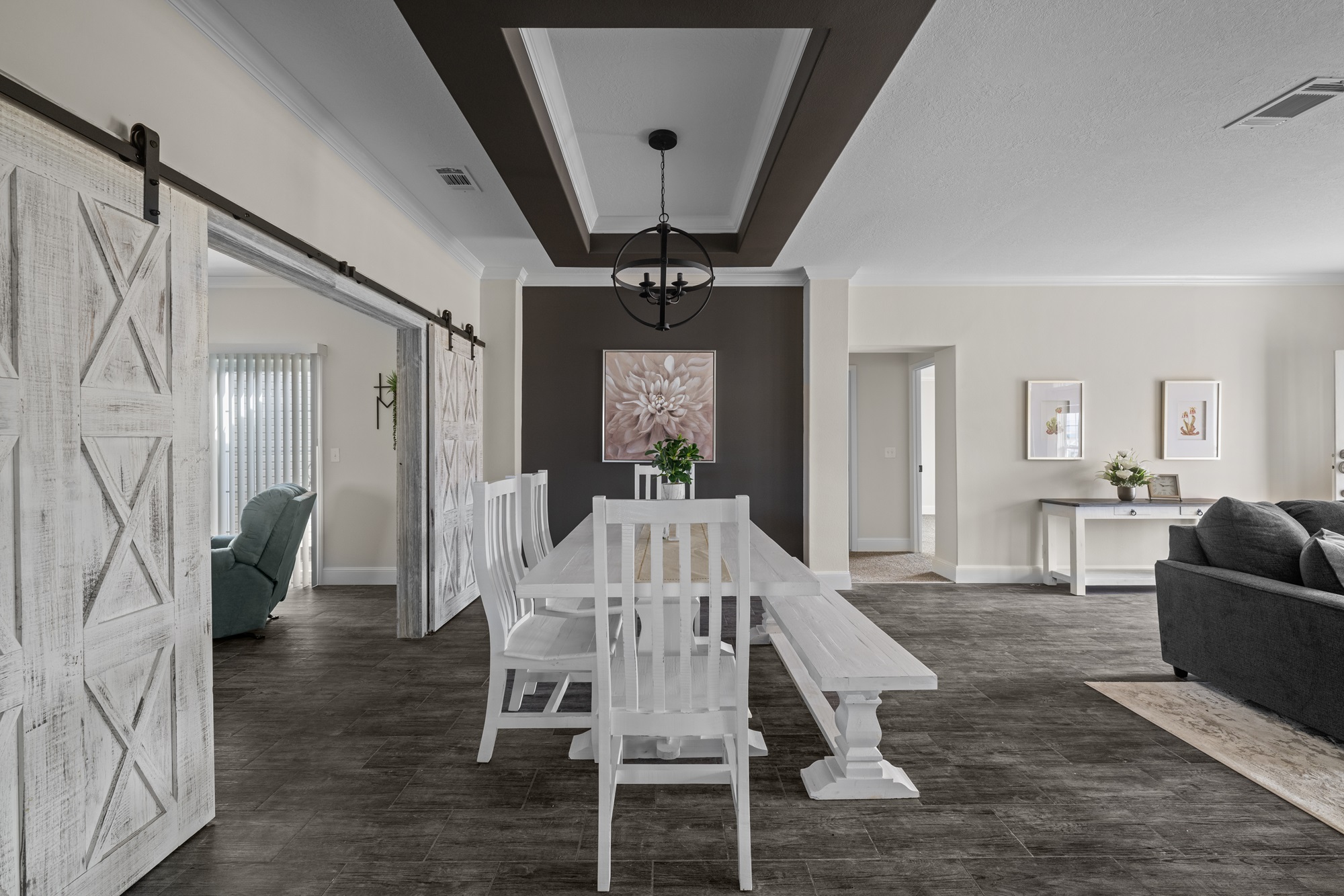 Spacious, modern dining room with a white table and chairs on dark wood flooring. Barn doors open to a sitting area. Art and plants add warmth.