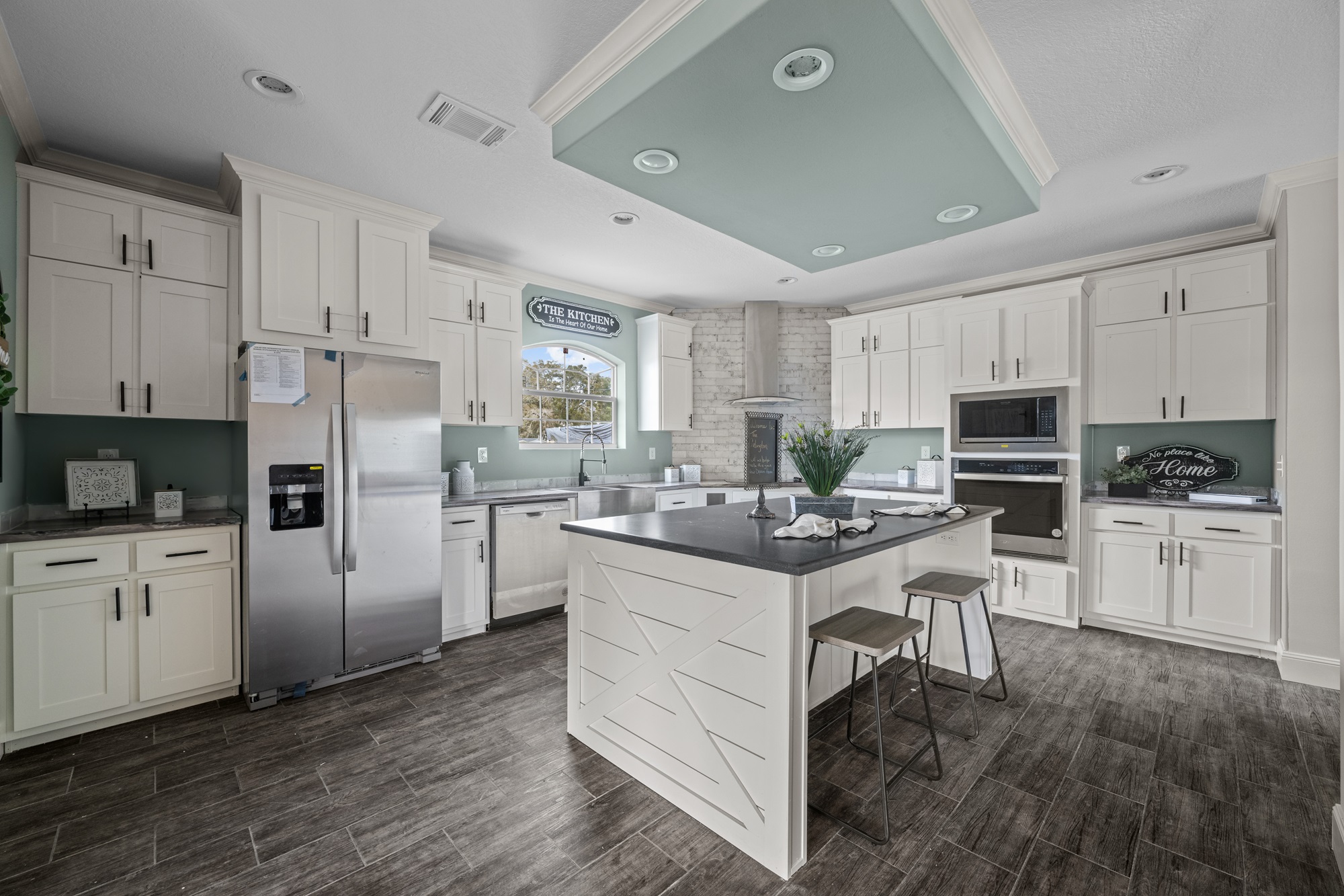 Spacious kitchen with light cabinets, a central island with stools, stainless steel fridge, and built-in oven. Green accents create a calm atmosphere.