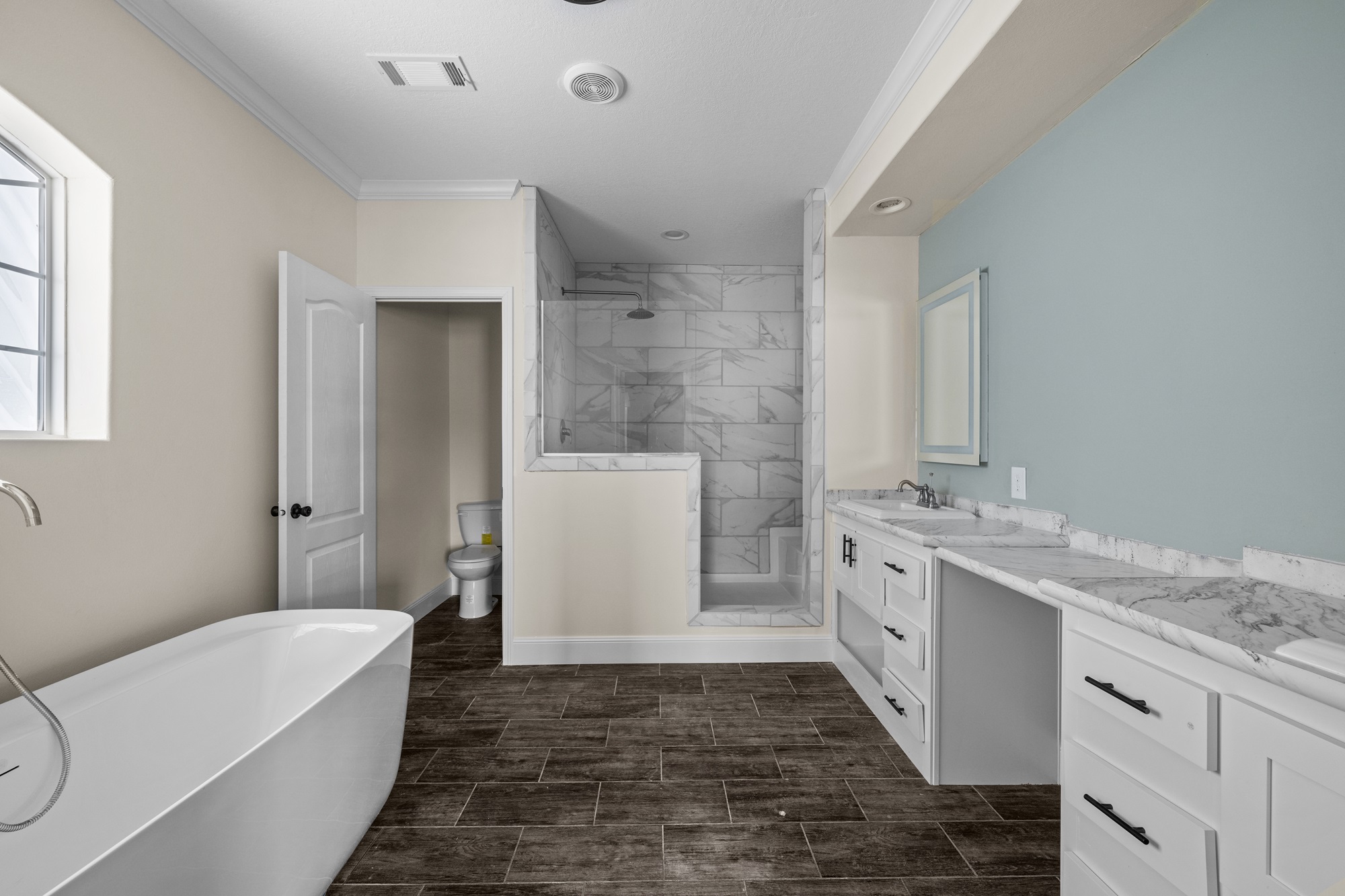 Spacious bathroom with a modern freestanding tub, glass-enclosed marble shower, dual sink vanity, and wooden floor, creating a calm and luxurious feel.