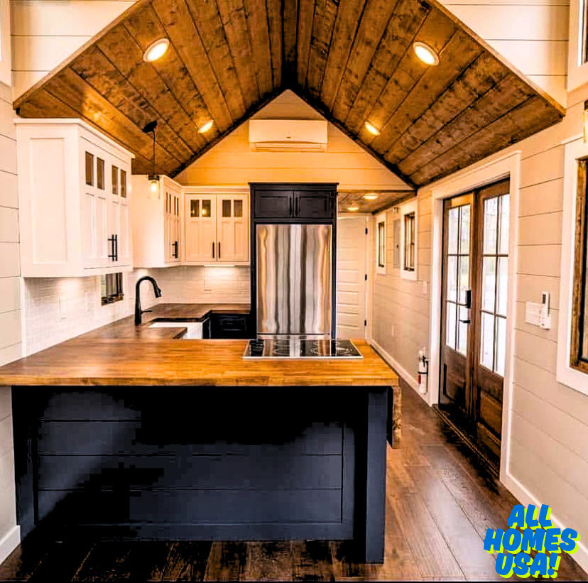 Rustic modern kitchen with wooden ceiling, white cabinets, black accents, and a central island. Warm lighting and wooden doors create a cozy atmosphere. Image for illustrative purposes.