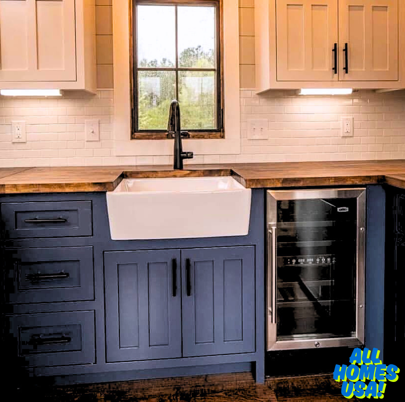 Modern kitchen with a farmhouse sink in a blue cabinet, wooden countertops, white tile backsplash, and a mini fridge. Bright and inviting vibe. Image for illustrative purposes.