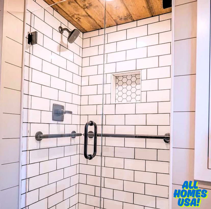 Modern shower with white subway tiles, glass door, and black fixtures. Wood ceiling adds warmth. Niche with hexagon tiles for storage. Cozy and stylish. Image for illustrative purposes.