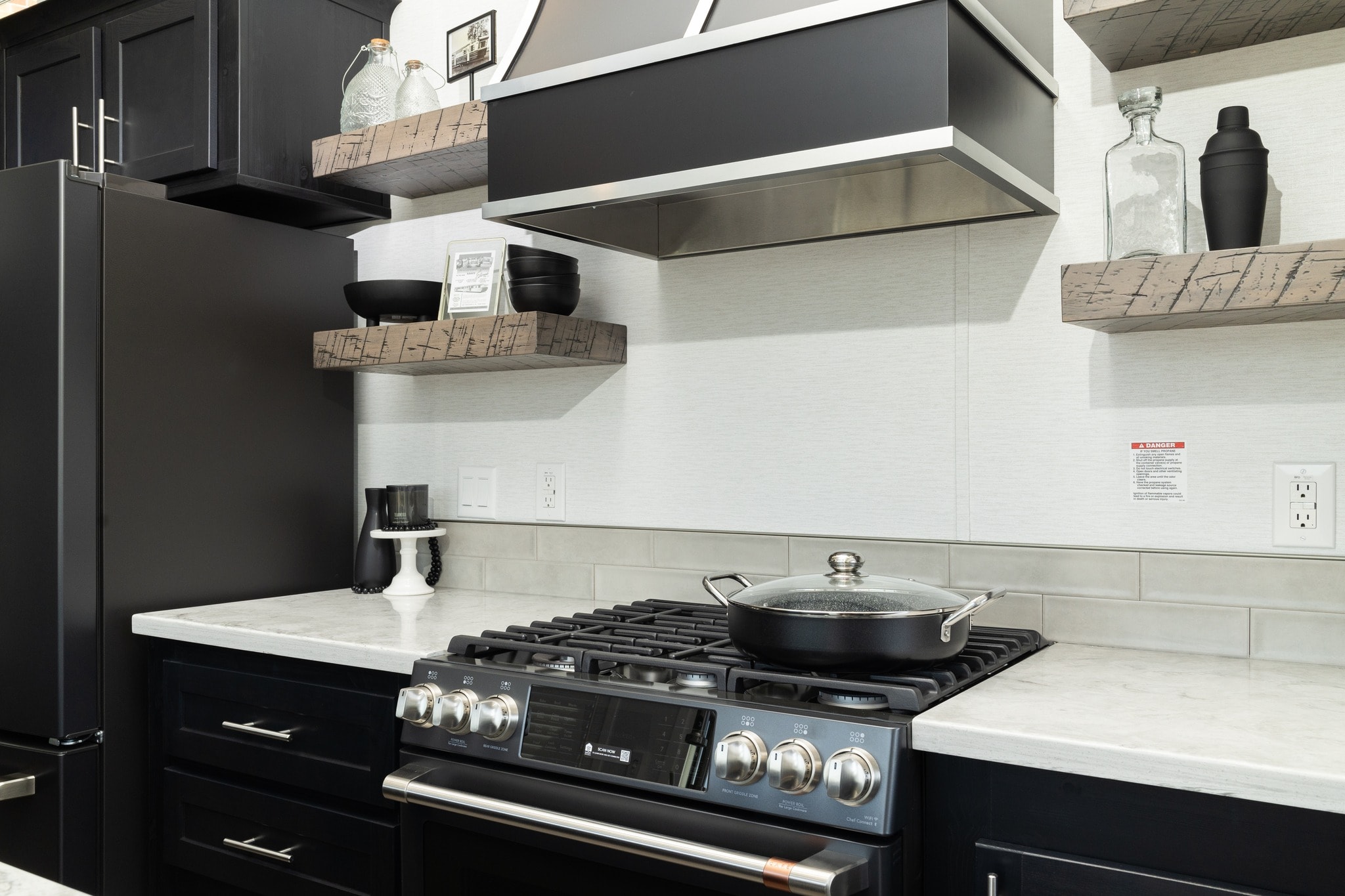 Modern kitchen with a sleek black stove, a pot with a glass lid, and wooden shelves holding black bowls and jars. The ambiance is clean and contemporary.