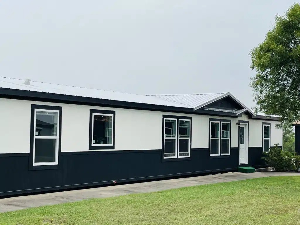 Single-story home with white and black exterior, six large windows, and a white door. It's set against a gray sky and green lawn, conveying a calm atmosphere.