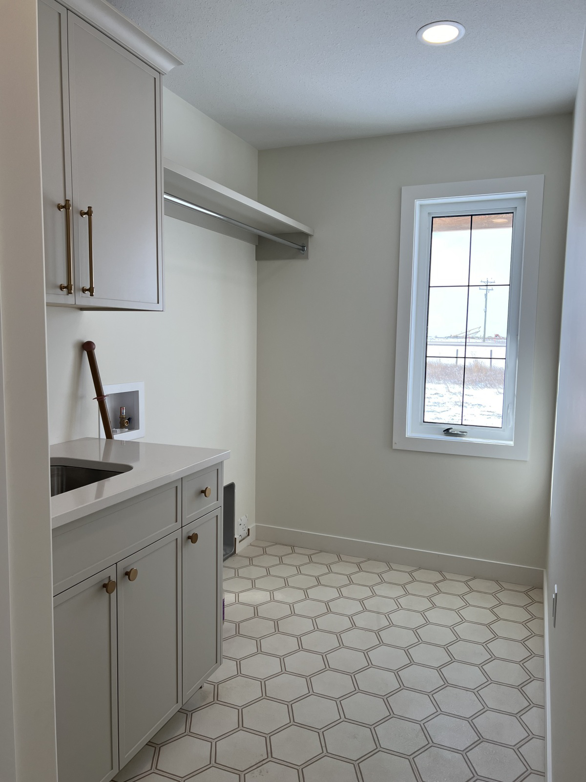 A bright, modern laundry room with hexagon tile flooring, white cabinets, a small sink, and a large window letting in natural light, creating a calm atmosphere.