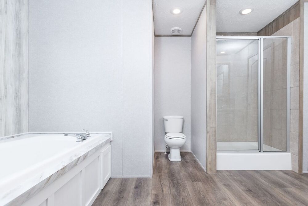 Modern bathroom with a white bathtub on the left, a toilet in the center, and a glass-enclosed shower on the right. Wooden flooring adds warmth.