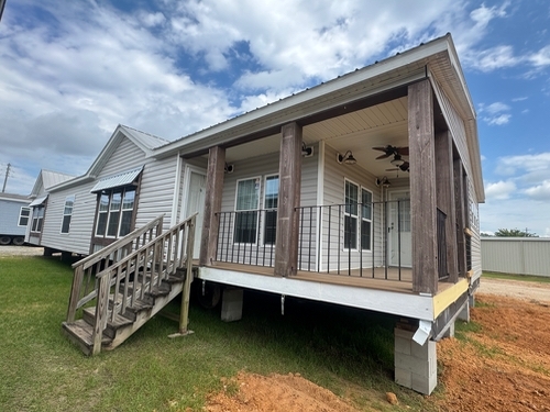 A white house with a raised wooden porch and stairs, set on a grassy area. The sky is partly cloudy, creating a calm and rustic atmosphere.