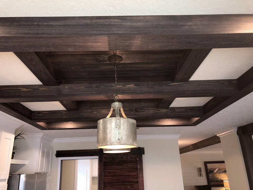 Ceiling with dark wood beams in a coffered pattern, featuring a rustic metal pendant light. The room is cozy and modern, with white walls and brown decor.