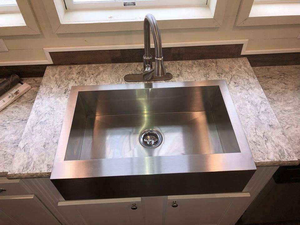 Stainless steel farmhouse sink with dual-handle faucet on a gray marbled countertop. Bright, clean, modern kitchen setting, evoking elegance and functionality.