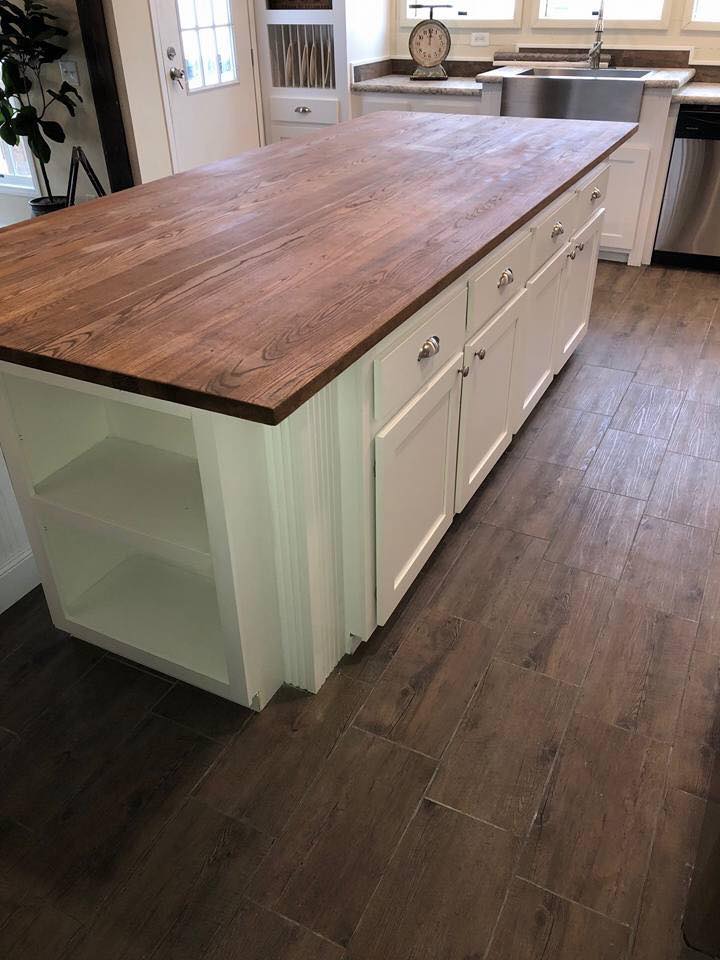 Spacious kitchen with a wooden island and white cabinets. The room features a farmhouse sink, patterned floor tiles, and a rustic, cozy ambiance.