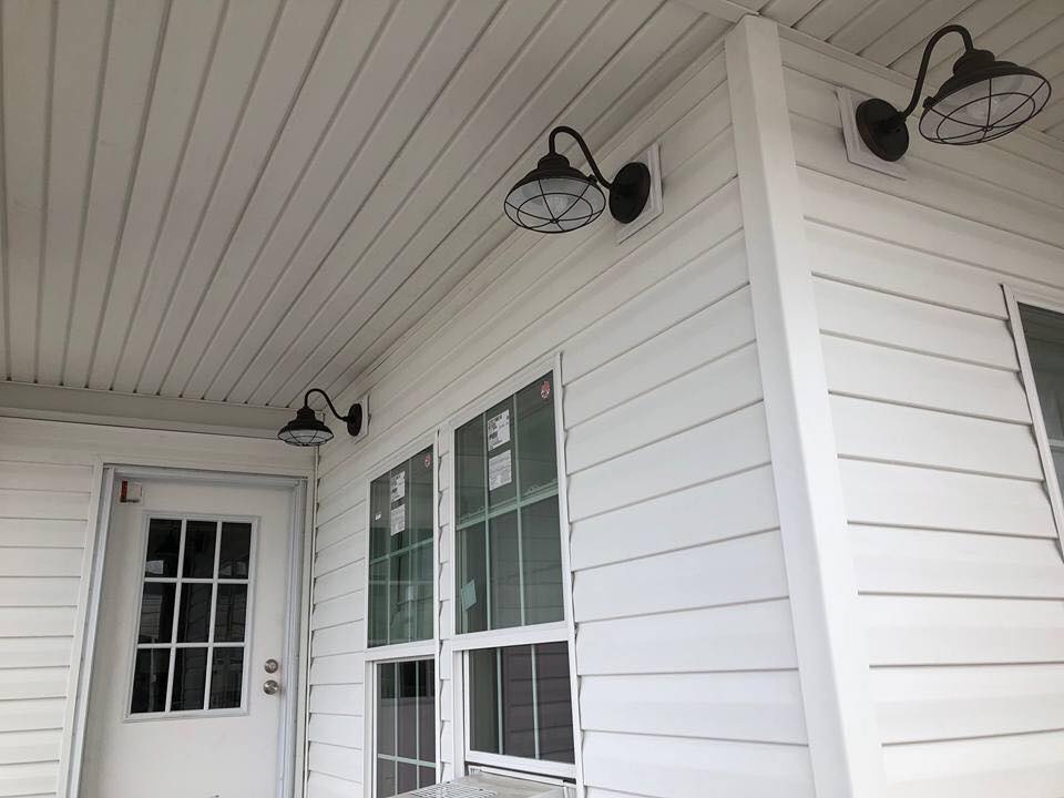 A white porch corner with modern black wall sconces, glass-paneled door, and adjacent large windows. The clean design creates a calm, inviting ambiance.