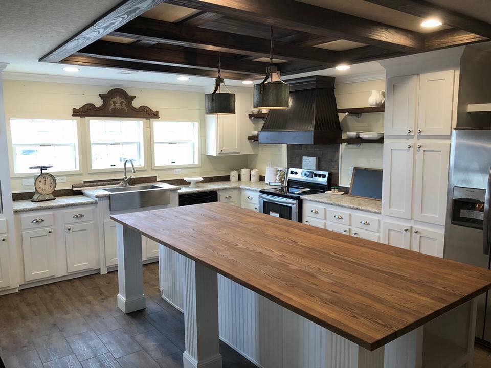 Spacious kitchen with white cabinets, a wooden island, and stainless steel appliances. Pendant lights hang from a wood-accented ceiling, creating a warm ambiance.