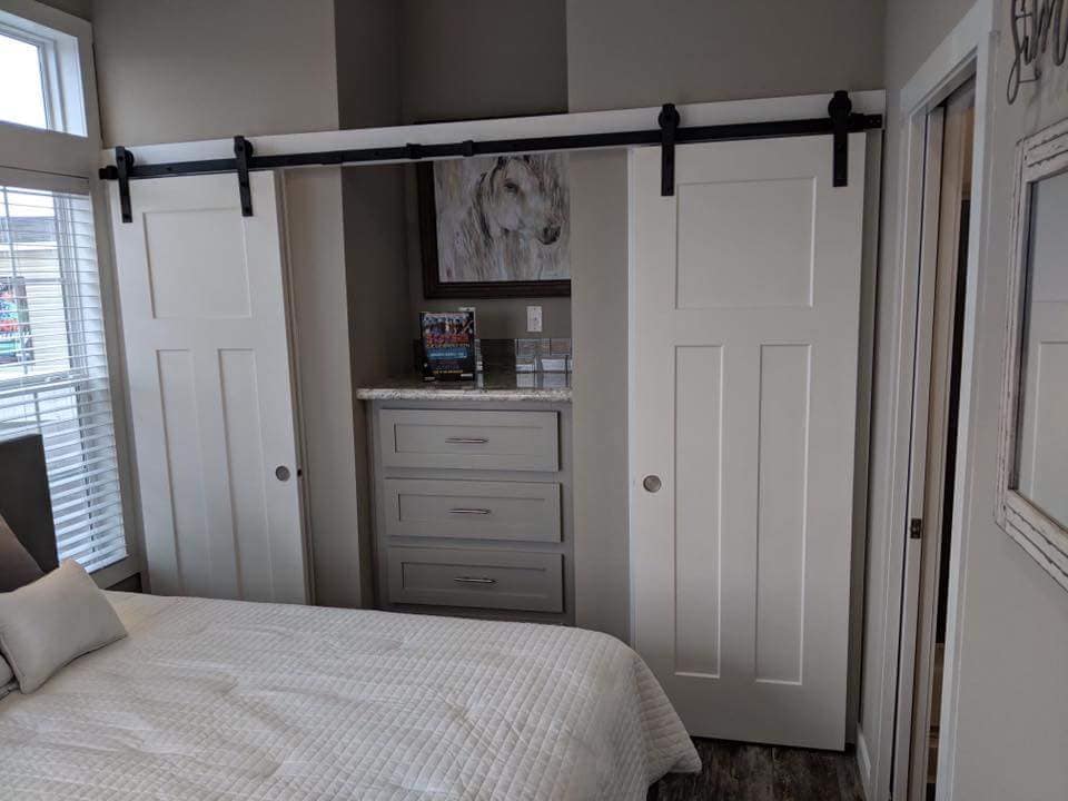 Bedroom with a quilted bed, sliding barn doors, and gray chest of drawers. A horse painting hangs above, creating a cozy, rustic atmosphere.