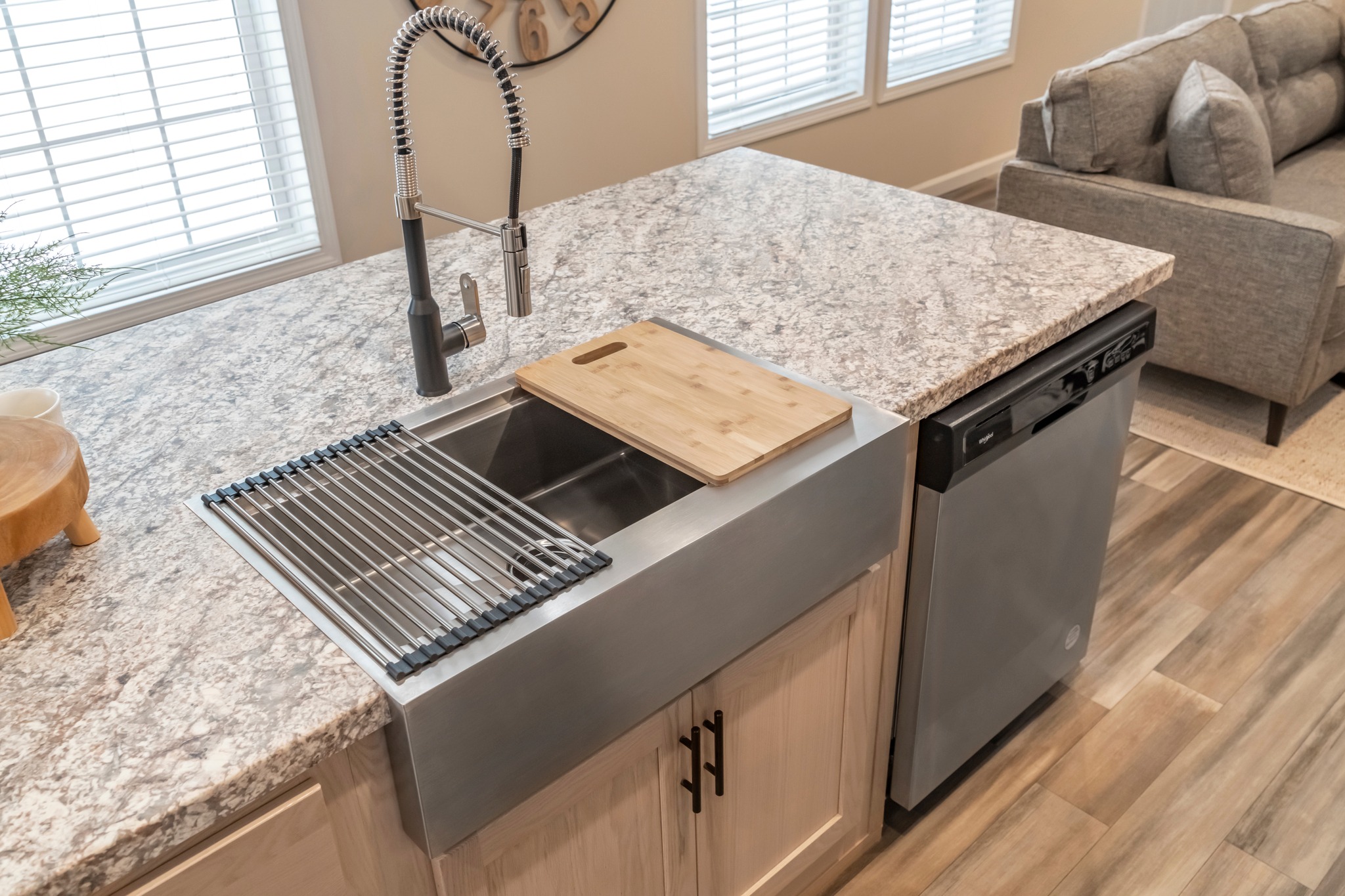 Modern kitchen with a marble countertop, stainless steel sink, and a tall faucet. A wooden cutting board and drying rack are placed over the sink.