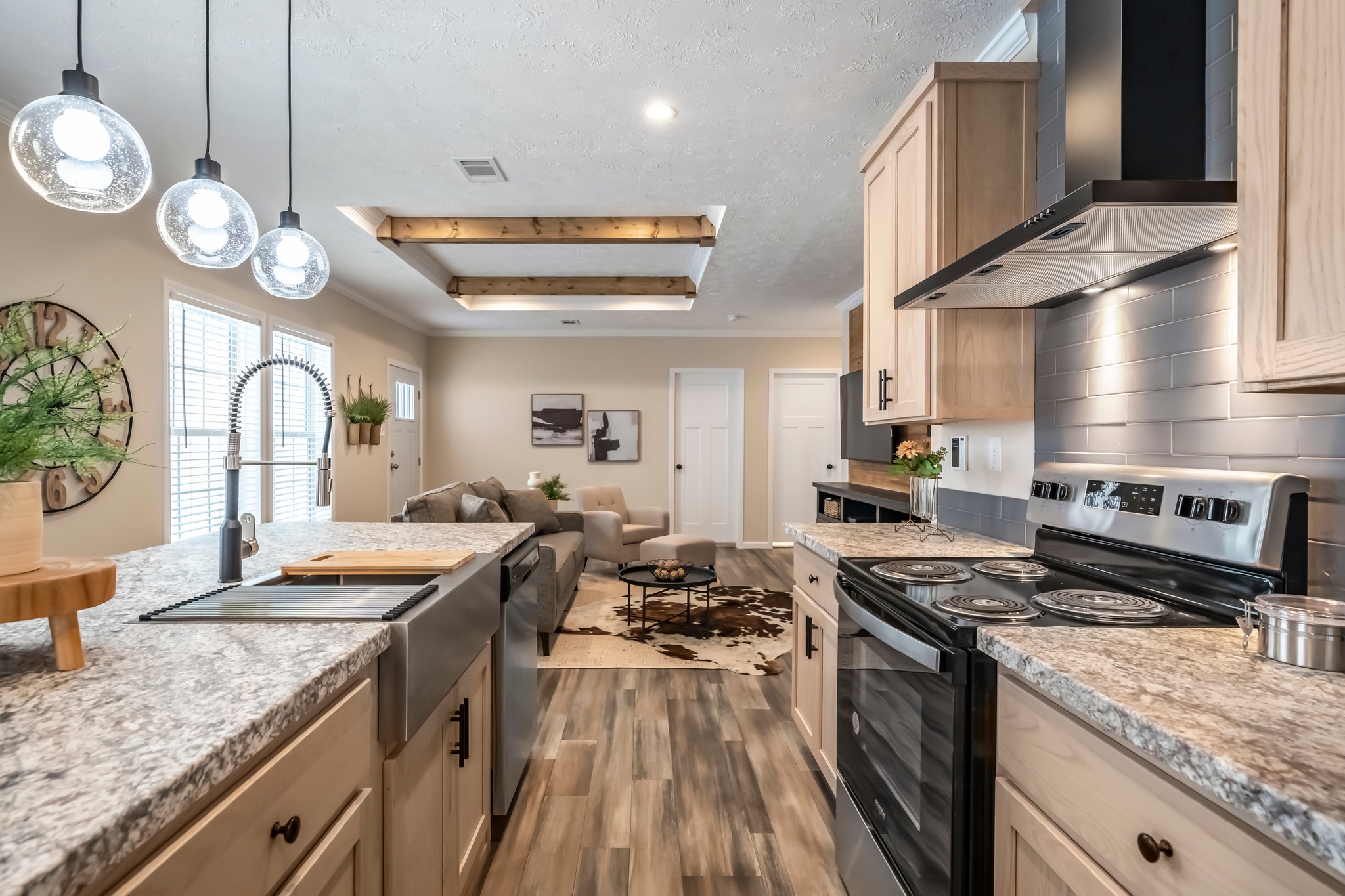 Stylish kitchen with granite countertops, pendant lights, and stainless steel appliances. Leads to cozy living room with neutral decor and wood accents.