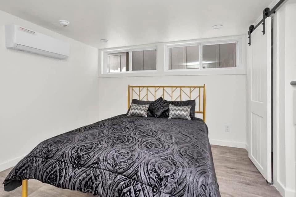A minimalist bedroom with a gold metal bed frame, patterned gray bedding, and stylish pillows. White walls and a barn door create a serene, modern atmosphere.