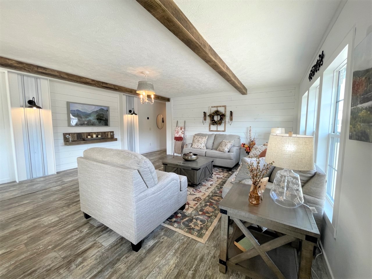Spacious living room with light gray sofas, rustic wooden beams, and shiplap walls. A cozy, inviting atmosphere with warm lighting and stylish décor.