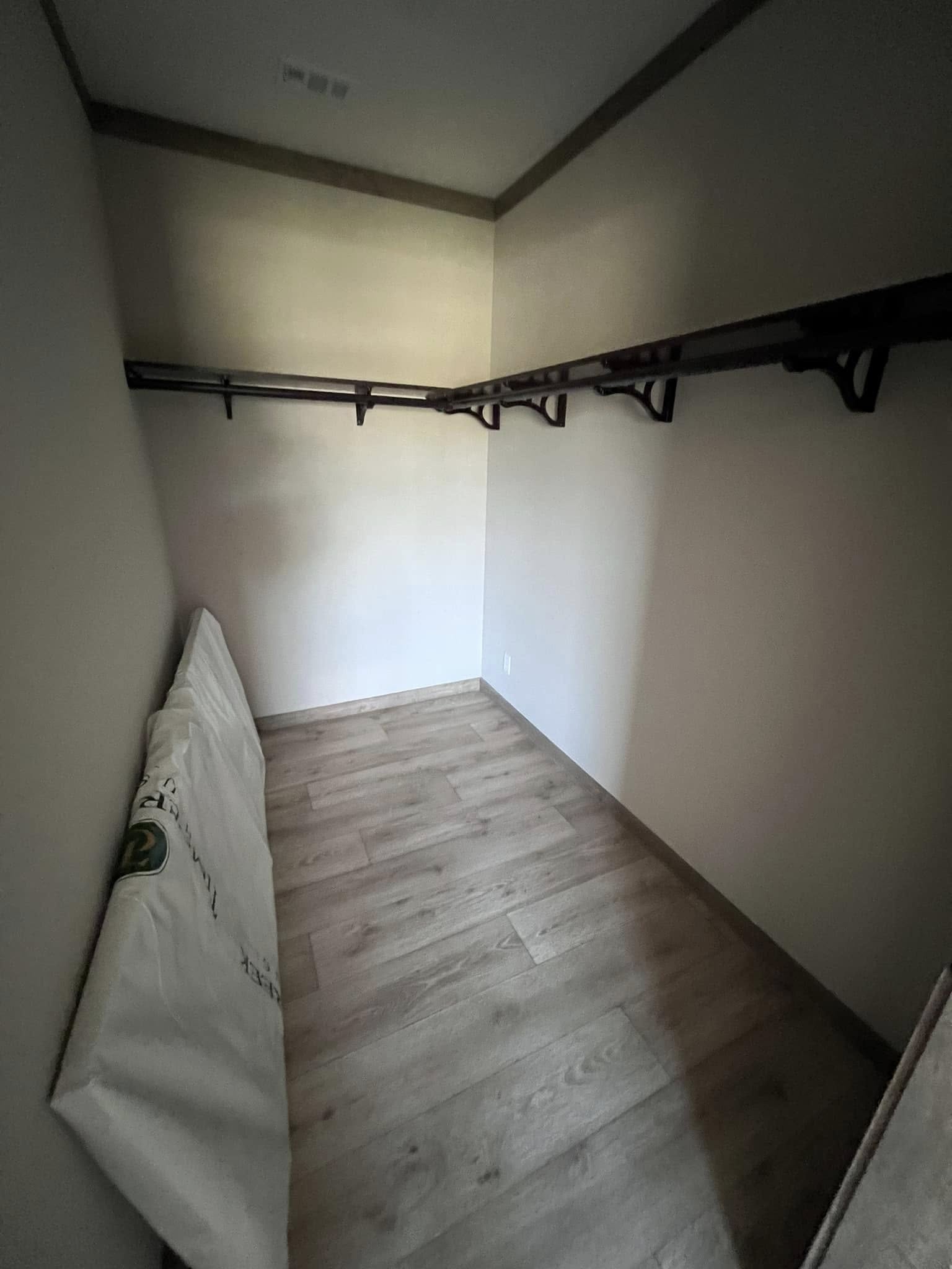 A small, empty walk-in closet with light wood flooring and wooden shelving on two sides. A folded blanket rests in the corner, creating a minimalist and tidy ambience.