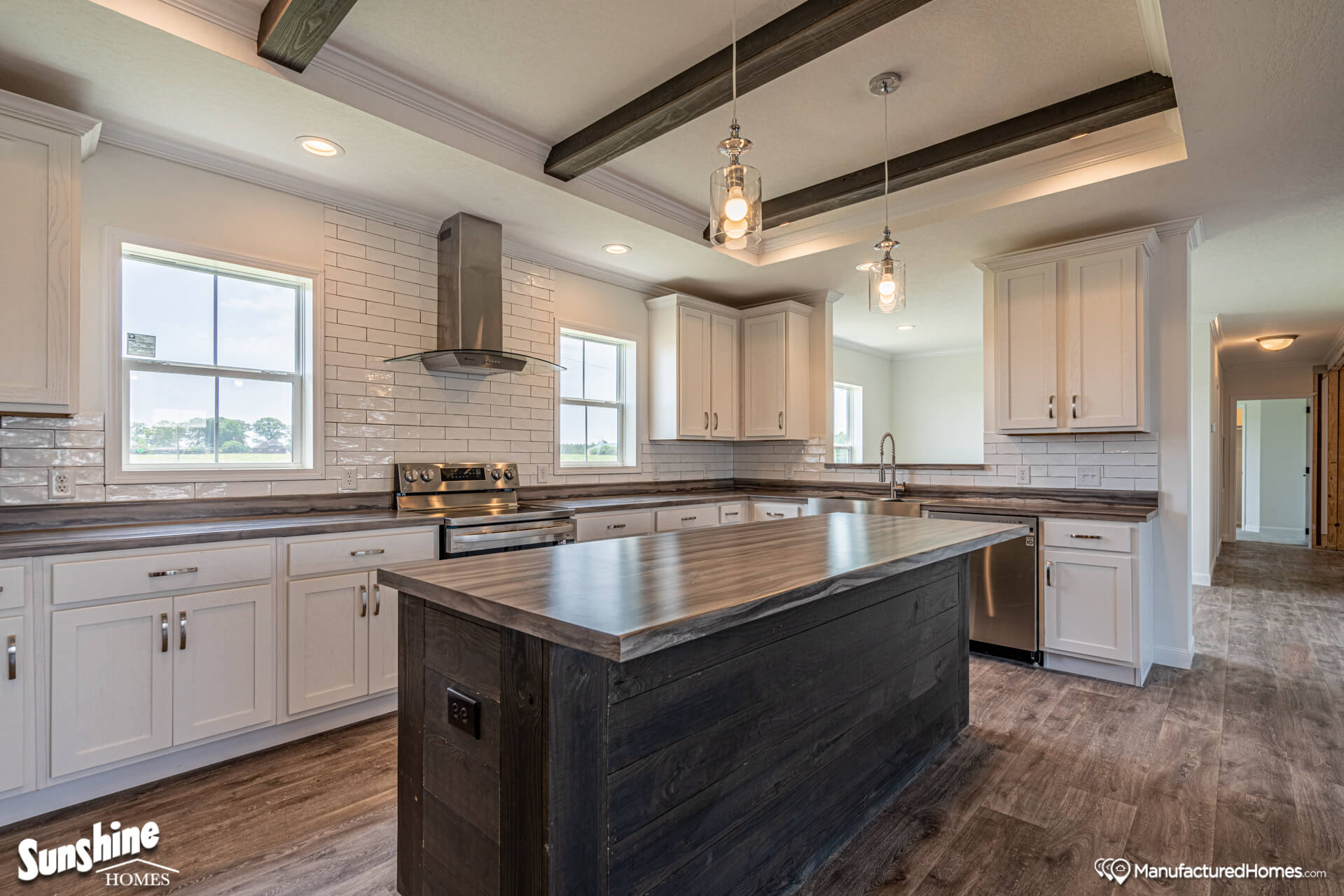Modern kitchen with wooden island, white cabinets, stainless steel appliances, and subway tile backsplash. Pendant lights and rustic beams add warmth.