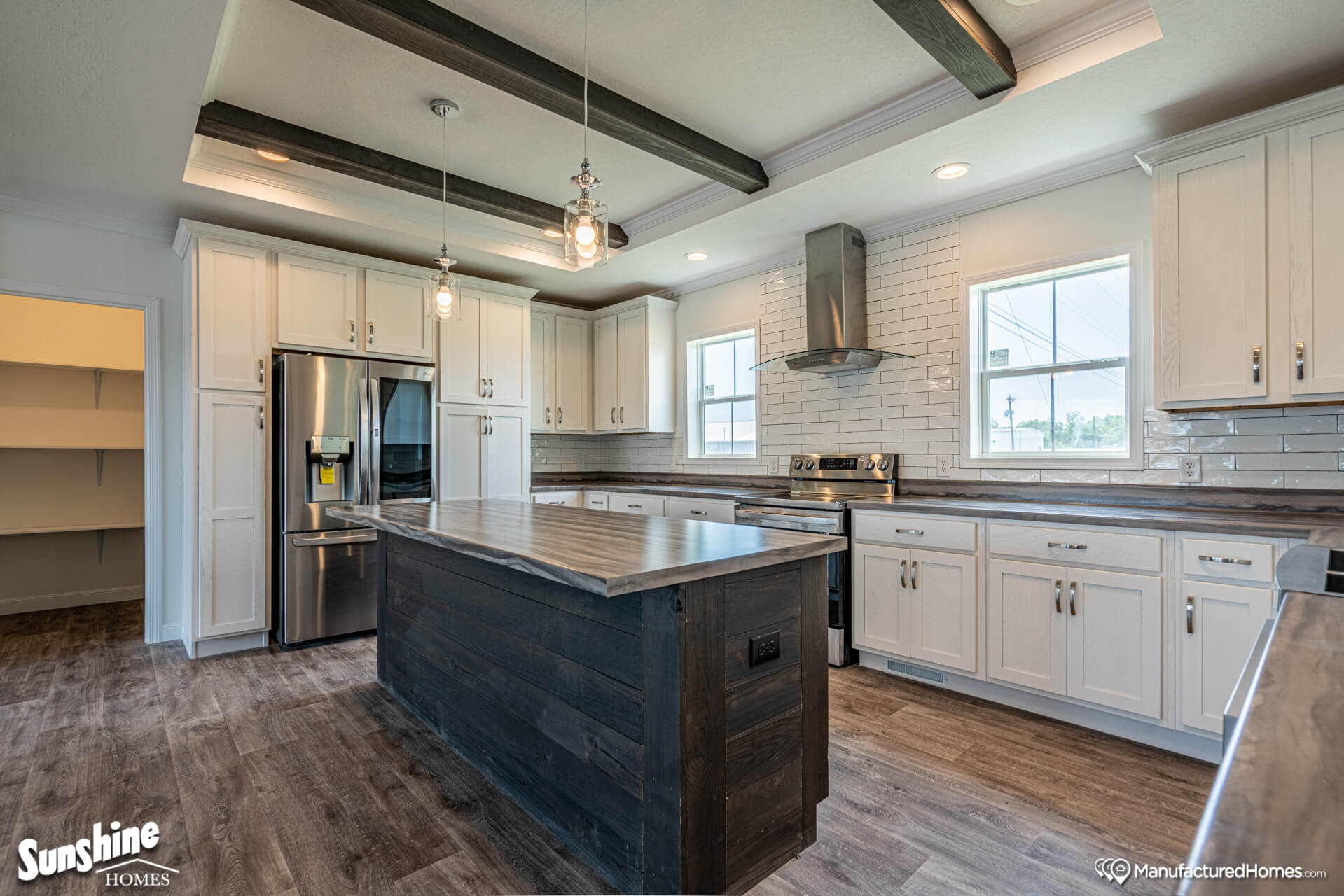 A modern kitchen with white cabinets, dark wooden beams, and an island. Stainless steel appliances, pendant lights, and a sleek range hood add elegance.