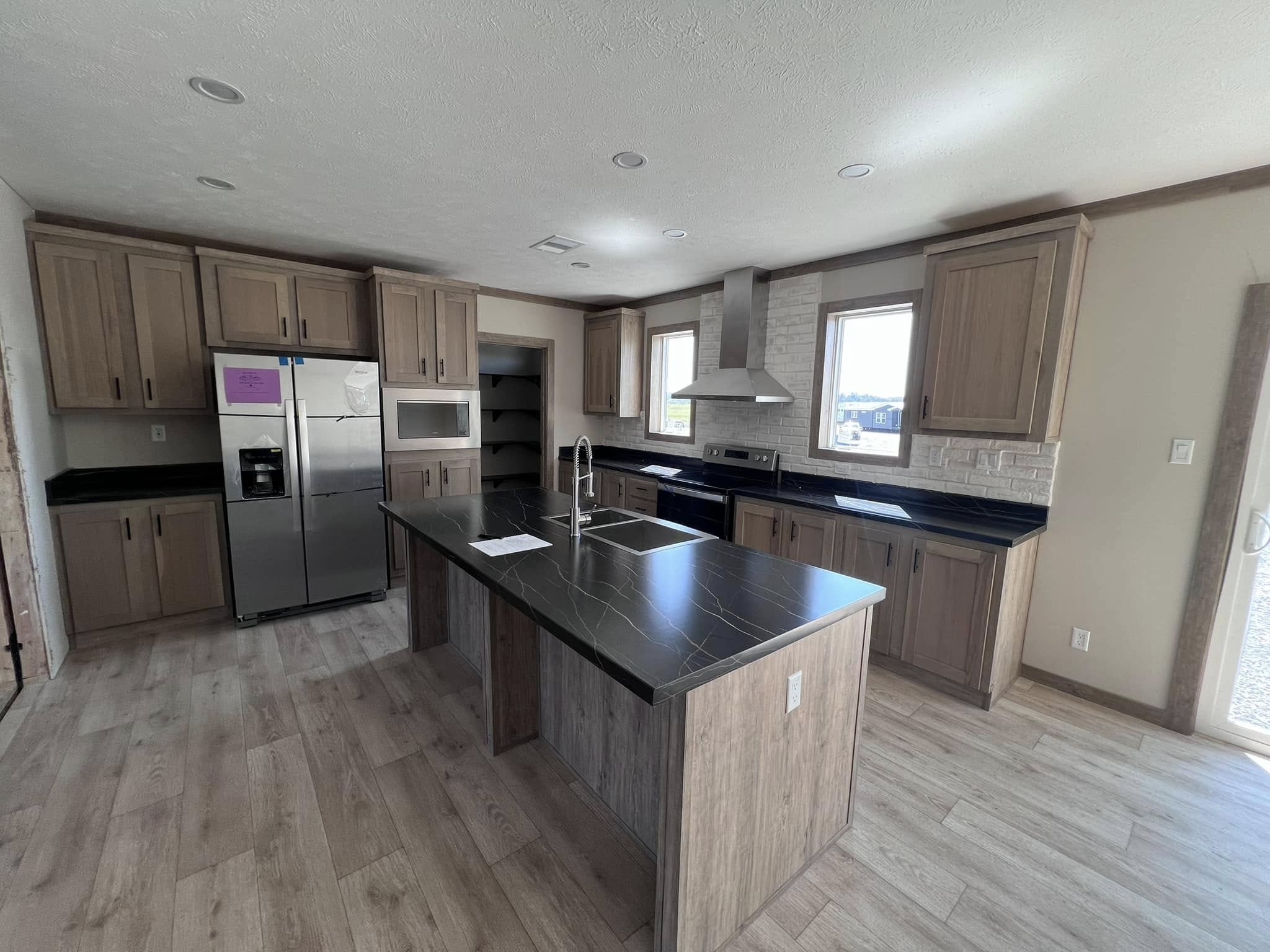 Modern kitchen with wooden cabinets, black marble countertops, and stainless steel appliances. An island with a sink enhances the spacious layout.