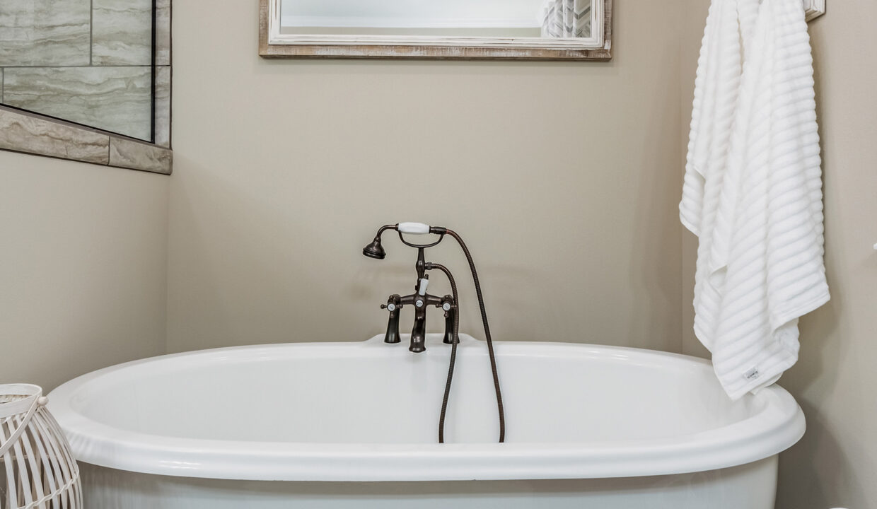 A white freestanding bathtub with vintage-style black faucet sits against a beige wall. A striped towel hangs nearby, conveying a cozy and relaxing ambiance.