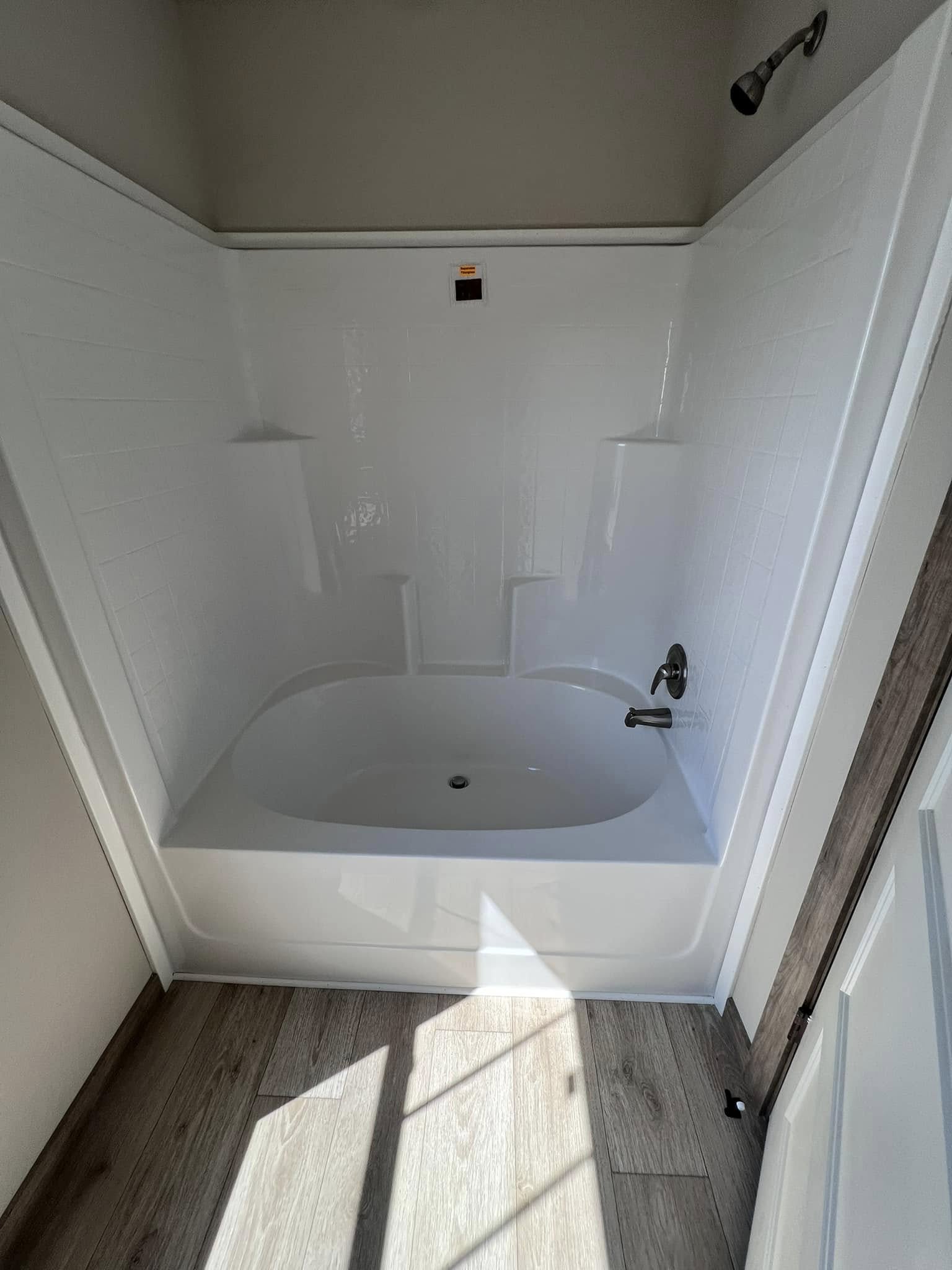 Modern bathroom with a white bathtub, sleek silver faucet, and tiled walls. Sunlight casts patterns on the wood-like floor, creating a serene ambiance.