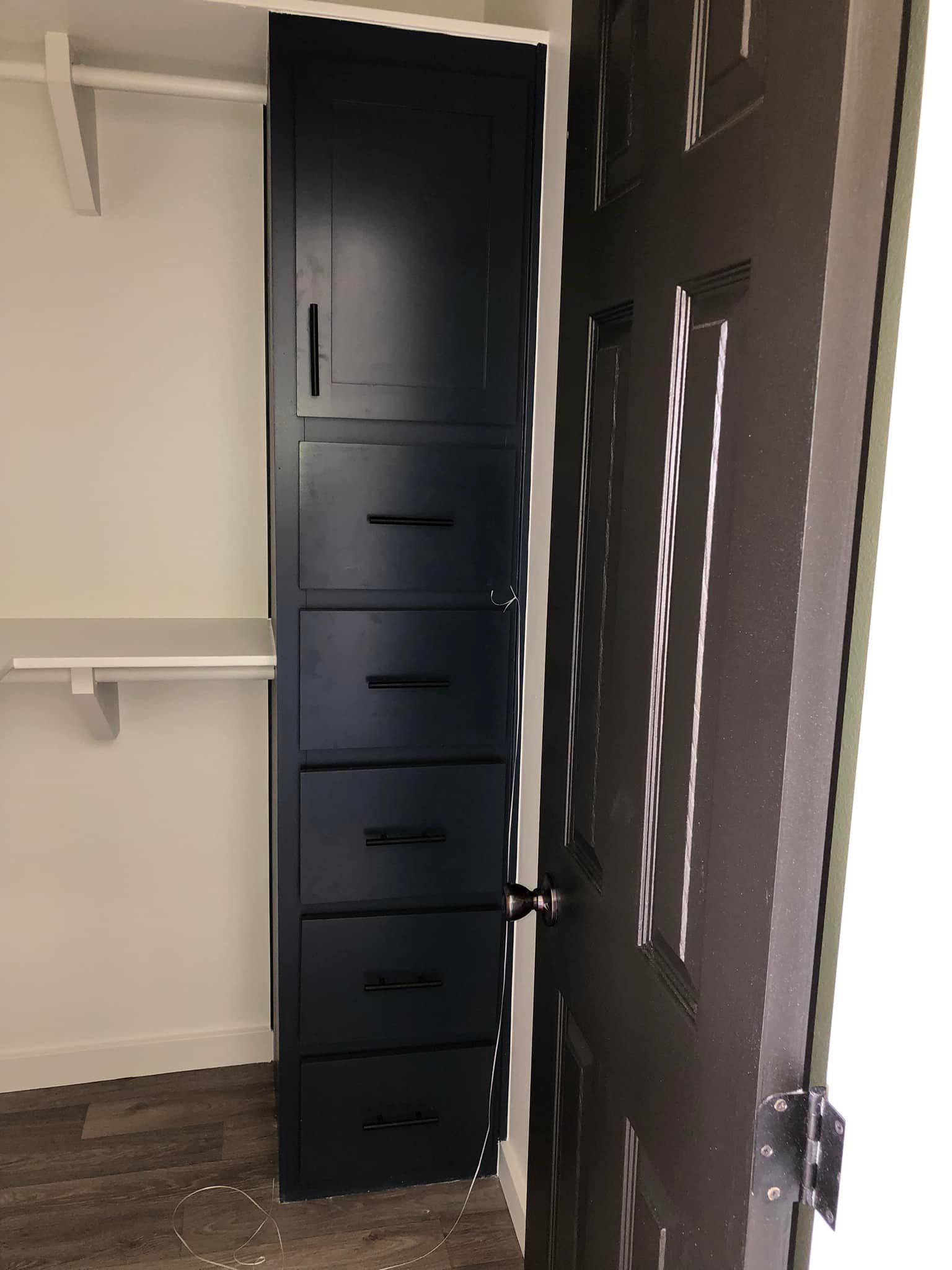 Narrow closet interior with a dark blue tall cabinet featuring multiple drawers. A partially open door blocks the cabinet, highlighting limited access.