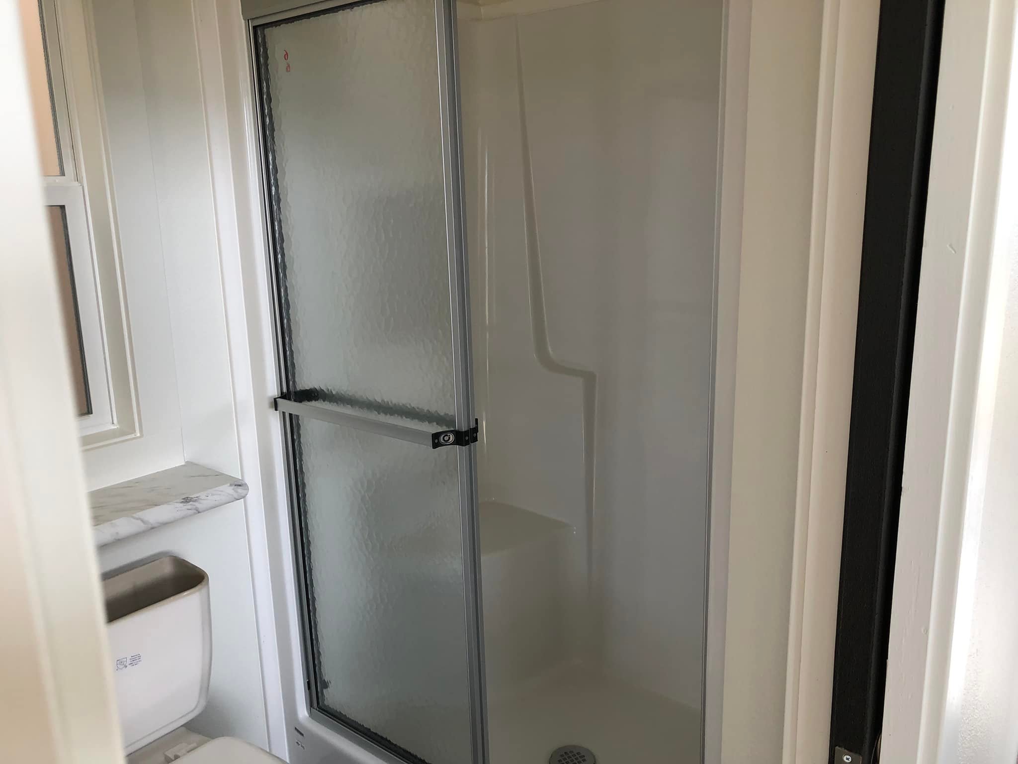 Small bathroom with a glass shower door, white walls, and a marble countertop. The setting is clean and minimal, conveying a tidy atmosphere.