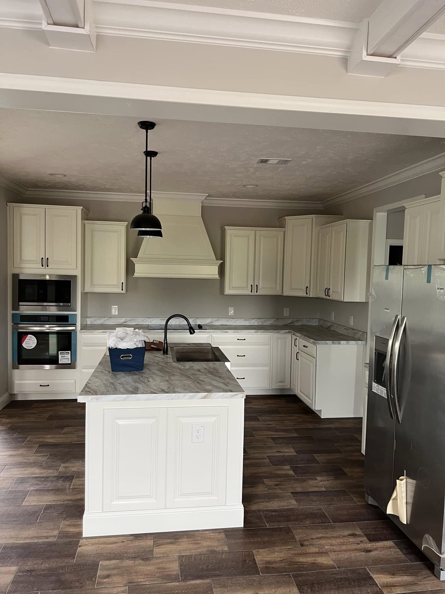 Spacious kitchen with white cabinets, marble countertops, and wood flooring. Features a central island, stainless steel appliances, and a pendant light.