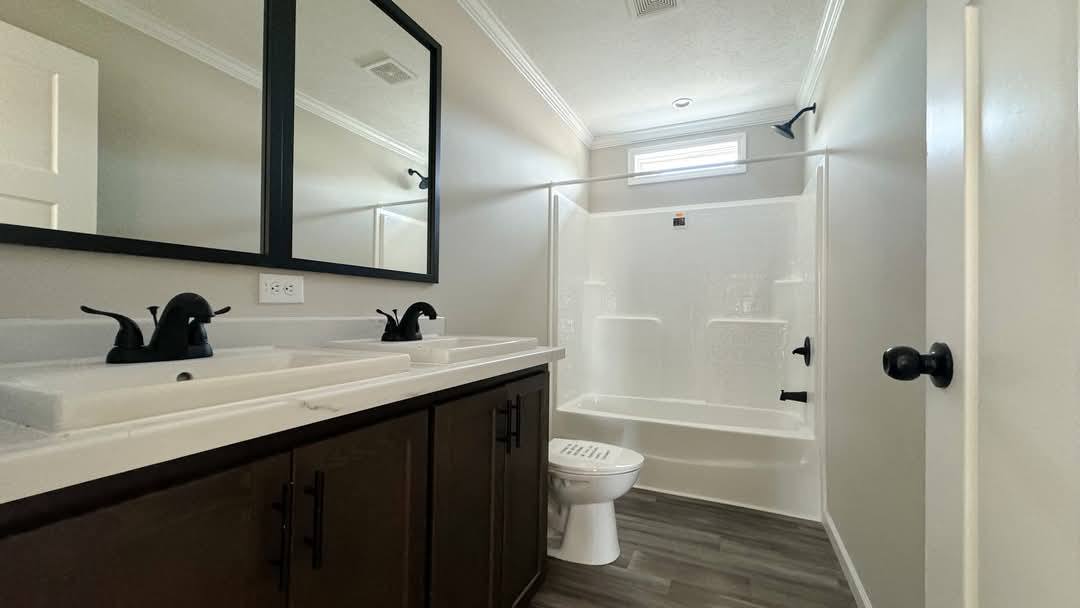 Modern bathroom with dual sinks, dark wood vanity, black faucet fixtures, large mirror, and a white bathtub under a small window. Neutral tones.