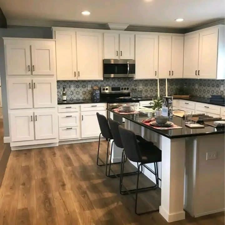 Modern kitchen with white cabinets, blue patterned backsplash, and wood flooring. Black countertop island with chairs and elegant tableware. Cozy ambiance.