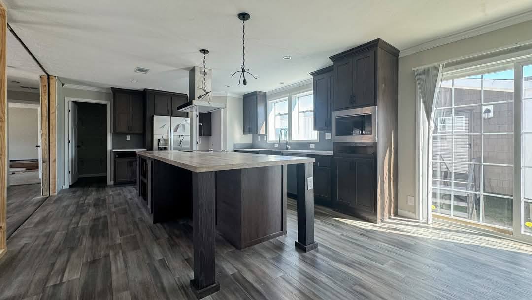 Spacious kitchen with dark wood cabinets, large island, and modern appliances. Sunlight pours in through a sliding glass door, creating a warm ambiance.