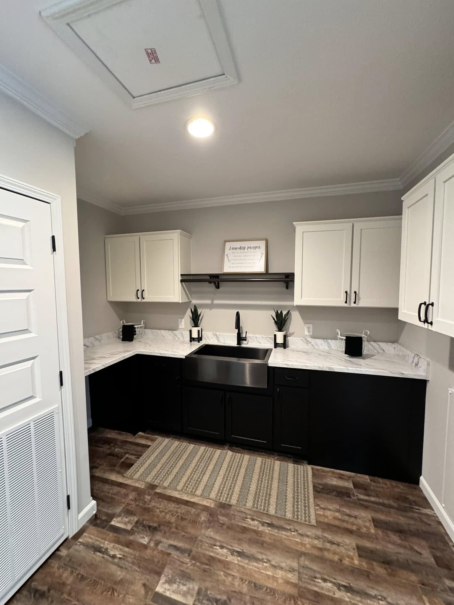 Modern kitchen with a farmhouse sink. Dark lower cabinets contrast with white upper ones. Marble countertops and small plants add elegance. Cozy ambiance.
