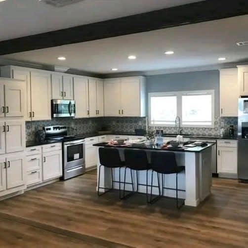 Modern kitchen with white cabinets, stainless steel appliances, and a central island. Wooden flooring and patterned tile backsplash add warmth.