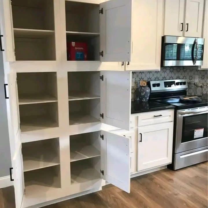 Empty white kitchen cabinets, one with a single box inside, stand open beside a black countertop and stainless steel oven. Modern and minimal.