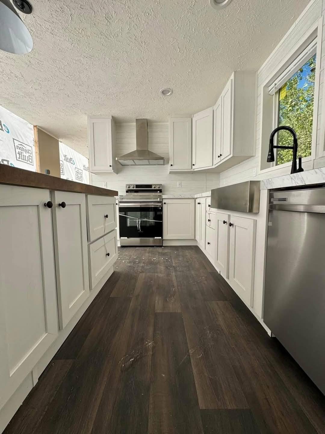 Modern kitchen with white cabinets, dark wood floors, stainless steel appliances, and a large window. Bright and sleek ambiance.