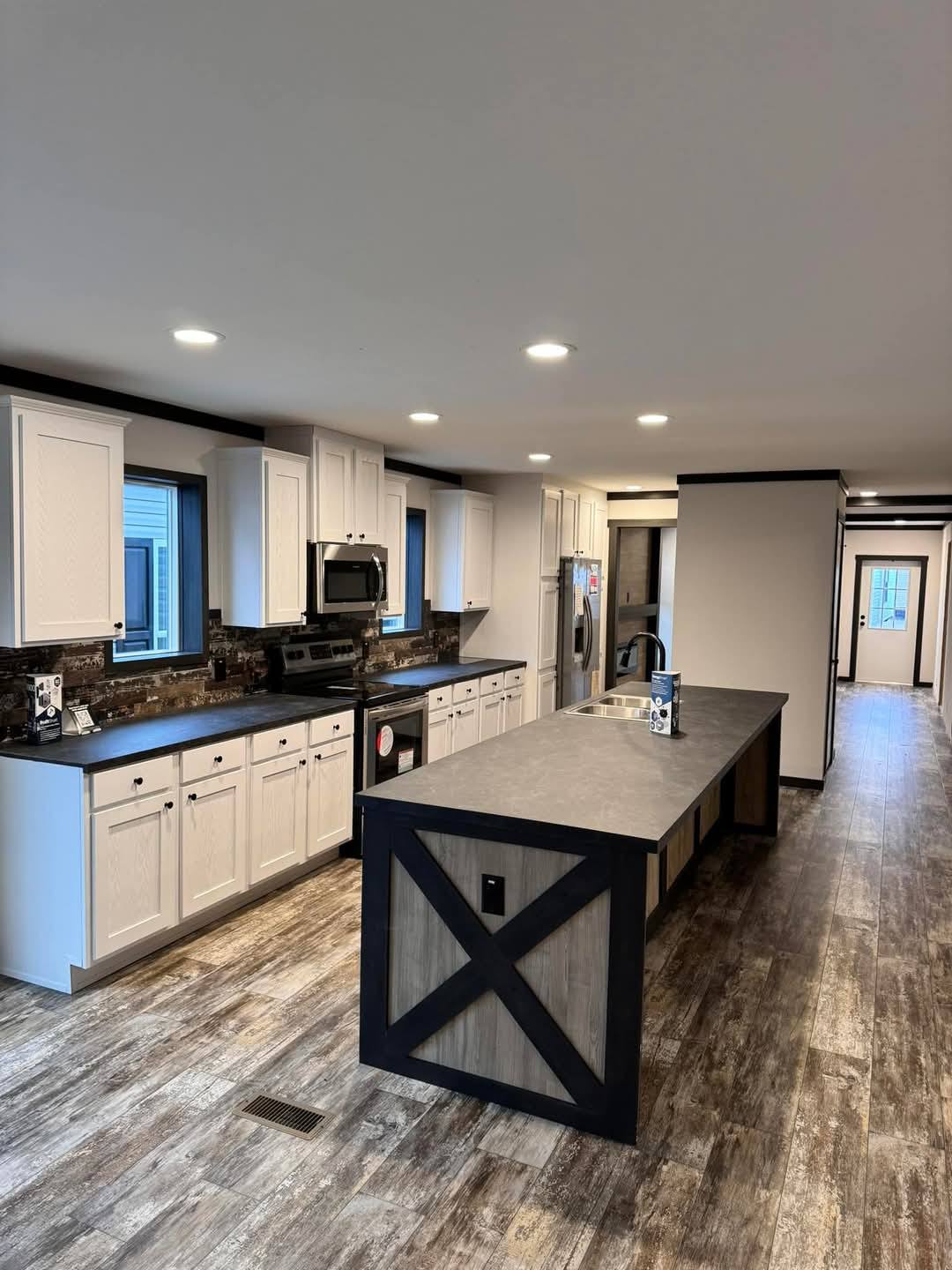 Spacious kitchen with white cabinets, dark countertops, and a long island. Wood-textured flooring and black and wood accents offer a modern, rustic vibe.