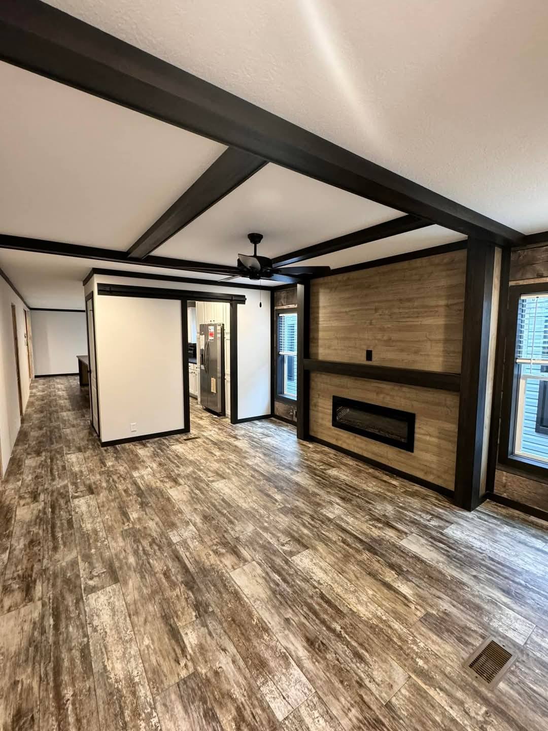 Spacious modern living room with gray wood floors, wood accent wall featuring a sleek, rectangular fireplace, and a ceiling fan. Bright and inviting ambiance.