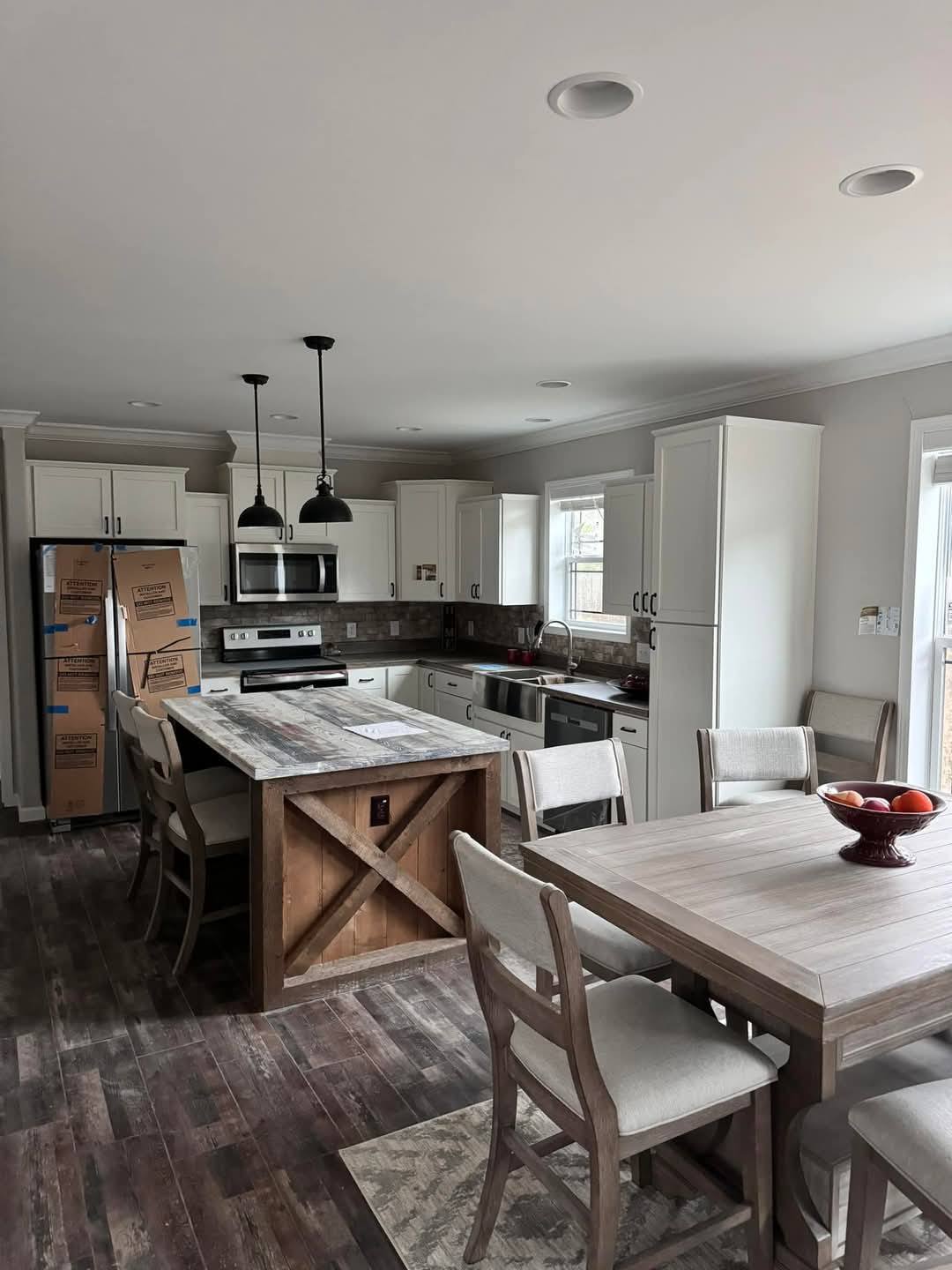 Modern kitchen with white cabinets, wooden floors, and a rustic island. Two pendant lights hang over the island. A dining table with chairs is nearby.