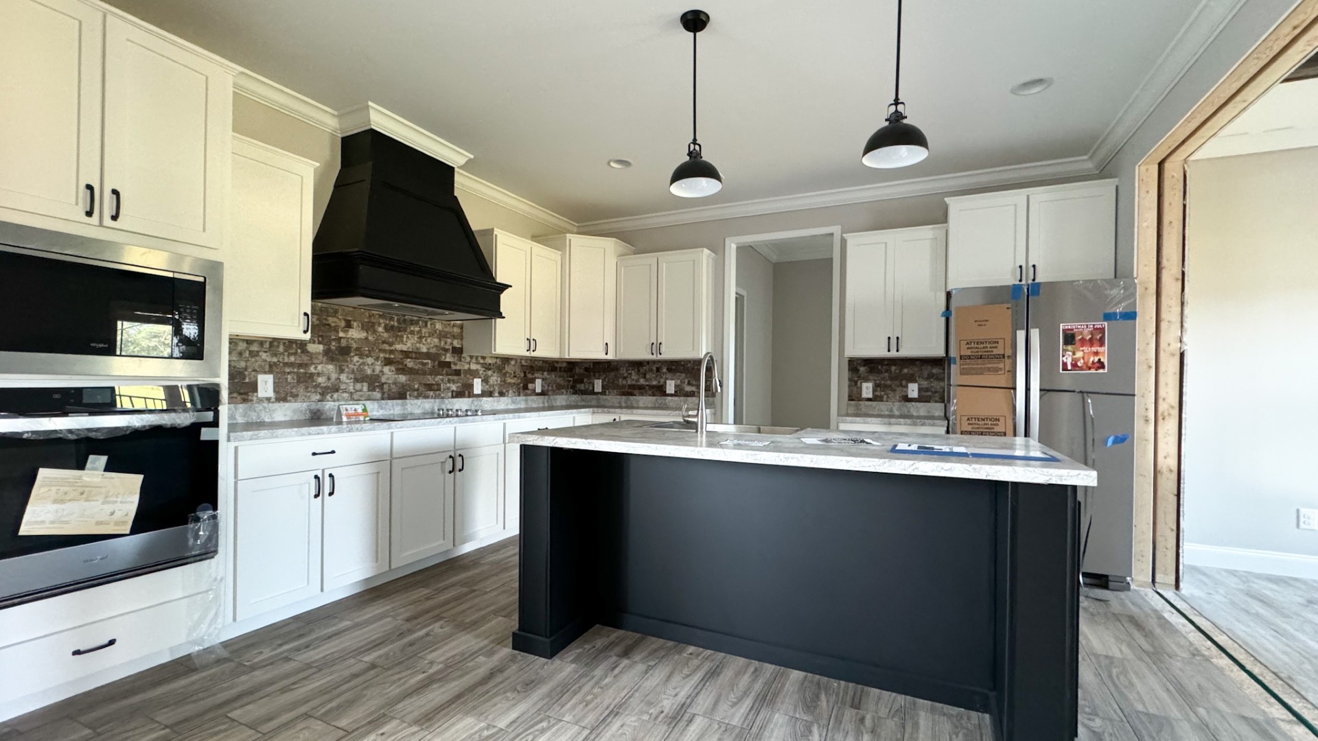 A modern kitchen with white cabinets, black accents, and a marble island. Brick backsplash, dual pendant lights, and wood flooring add warmth.