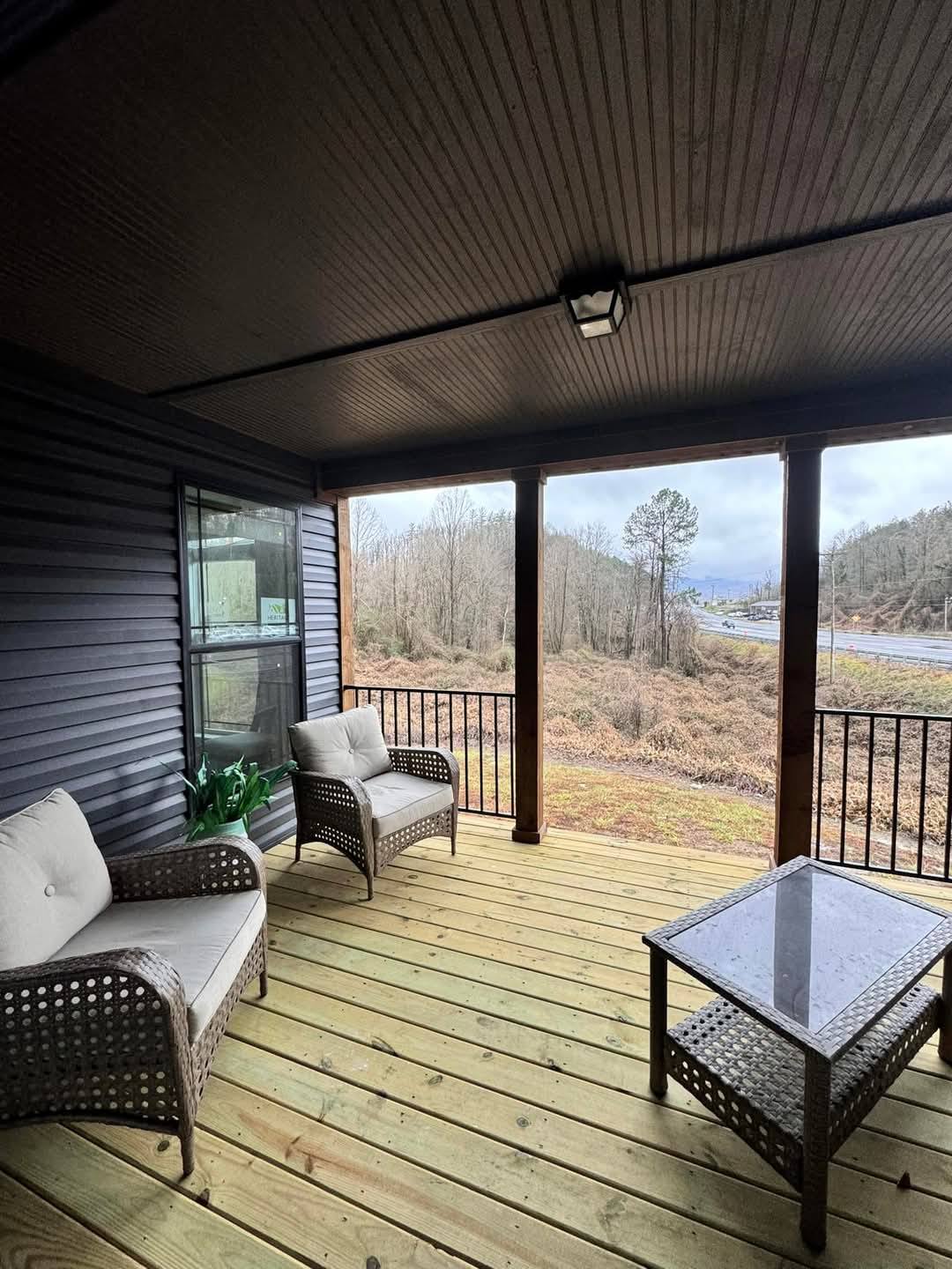 Covered porch with wicker furniture and cushions overlooking a serene wooded landscape. Overcast sky adds a tranquil, cozy atmosphere.