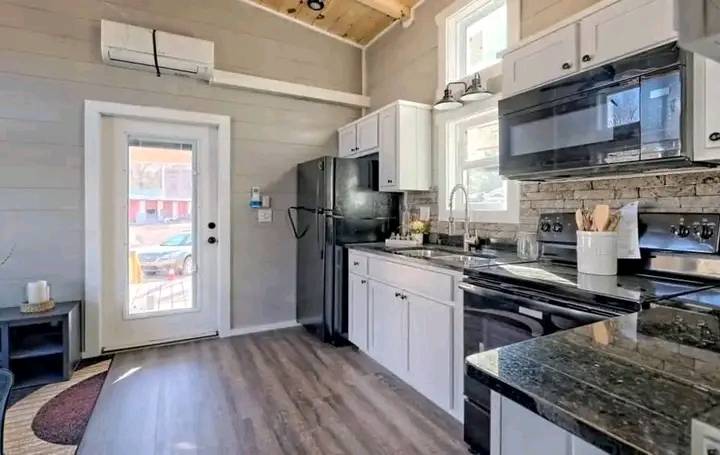 Modern kitchen in neutral tones with white cabinets, dark granite countertops, stainless steel appliances, and a door leading outside. Bright and inviting.