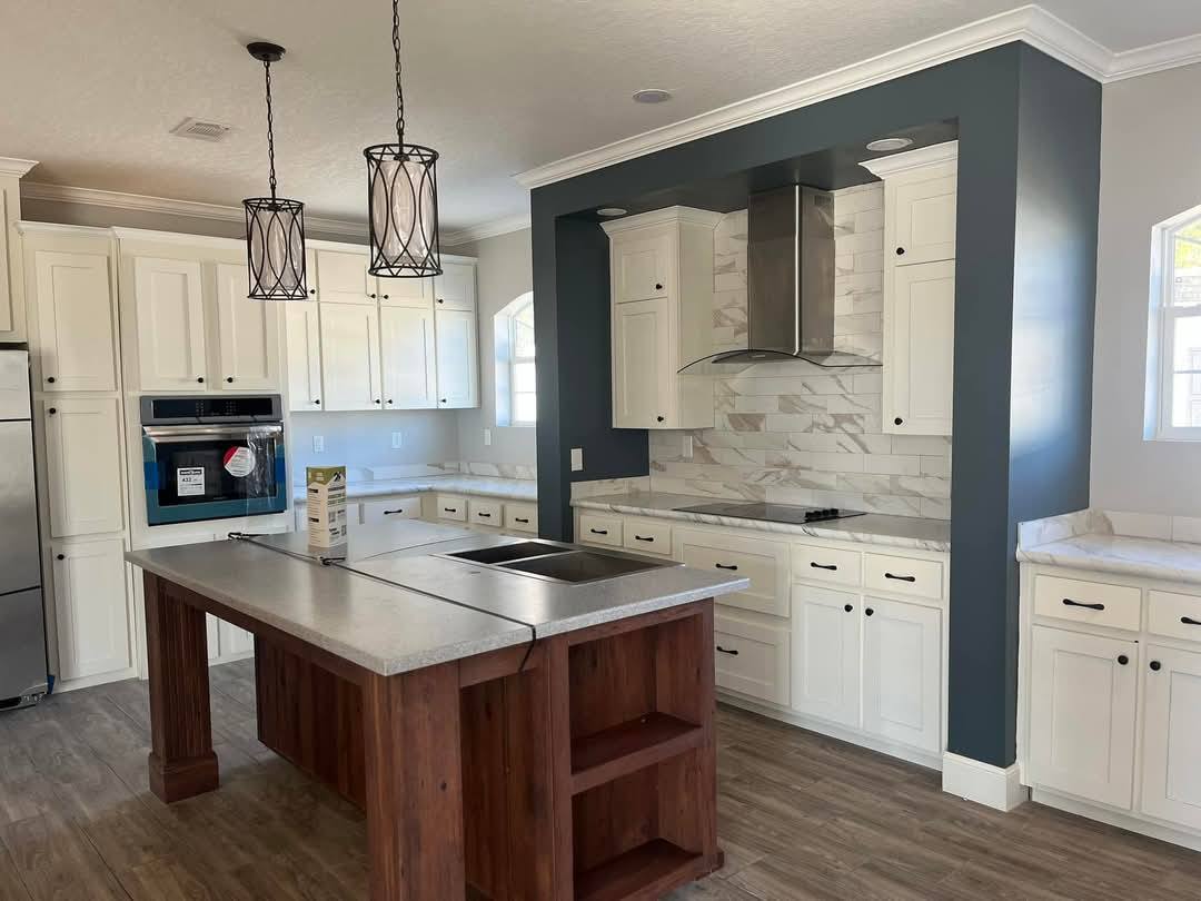 Modern kitchen with white cabinets, marble backsplash, and stainless steel appliances. A central island with a sink and two pendant lights above.