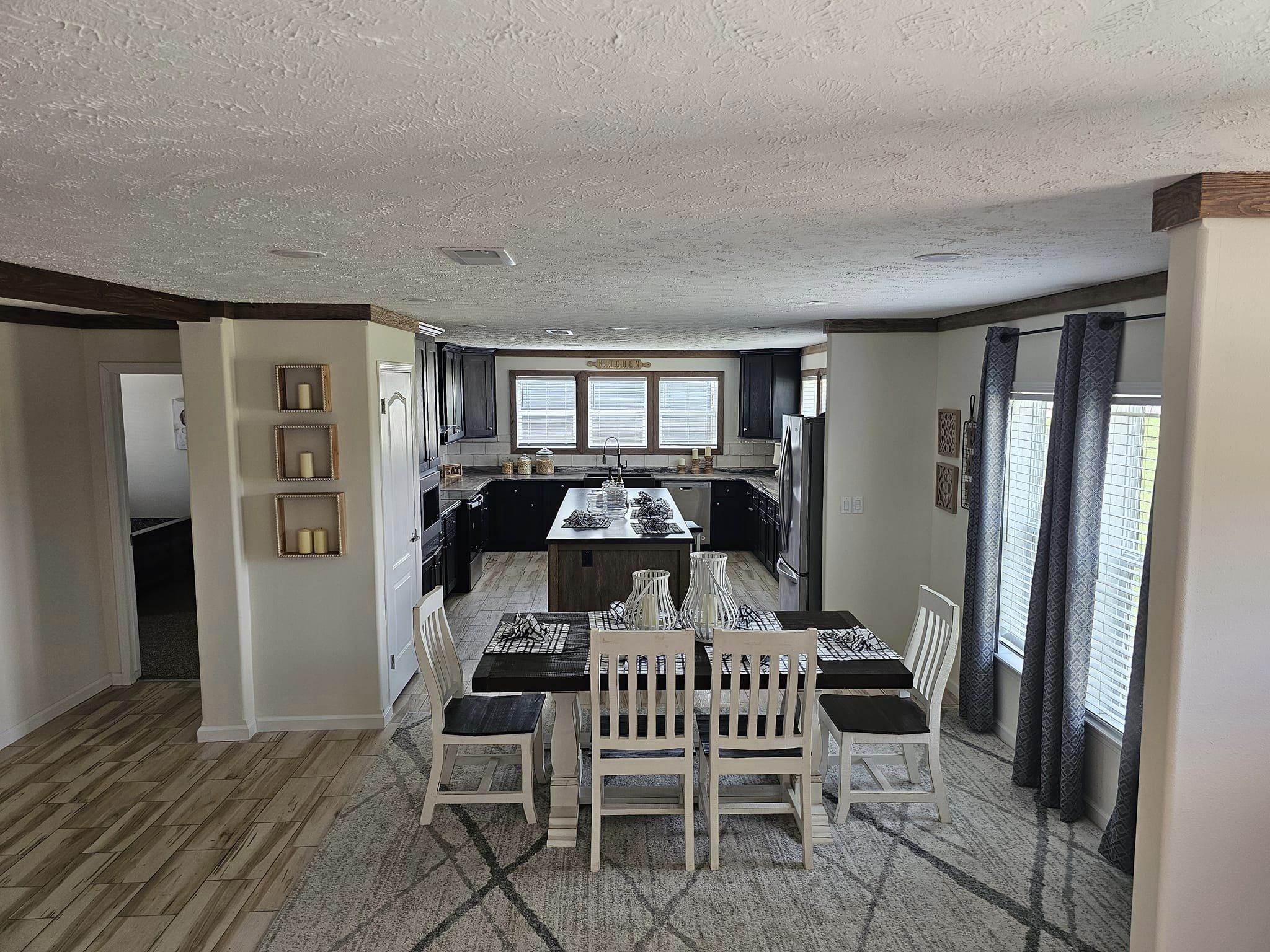 Spacious kitchen and dining area with a light wood floor, dark cabinets, central island, and a wooden table set for six. Bright, inviting ambiance.