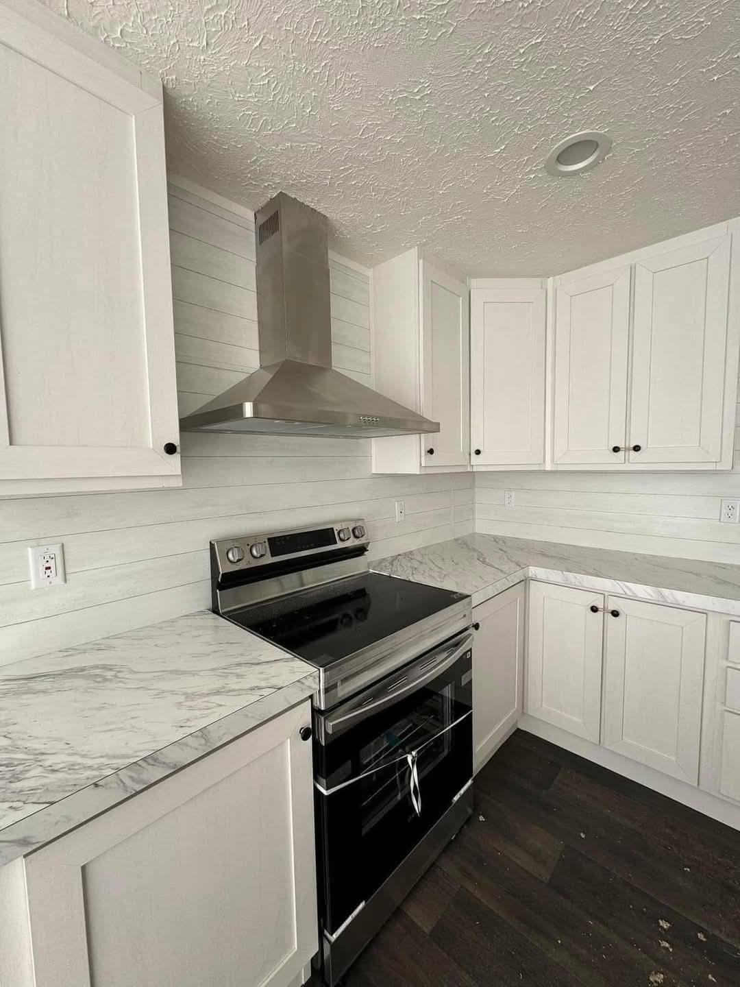 Modern kitchen with white cabinets, marble countertops, and a stainless steel stove with a matching range hood. The space is sleek and bright.