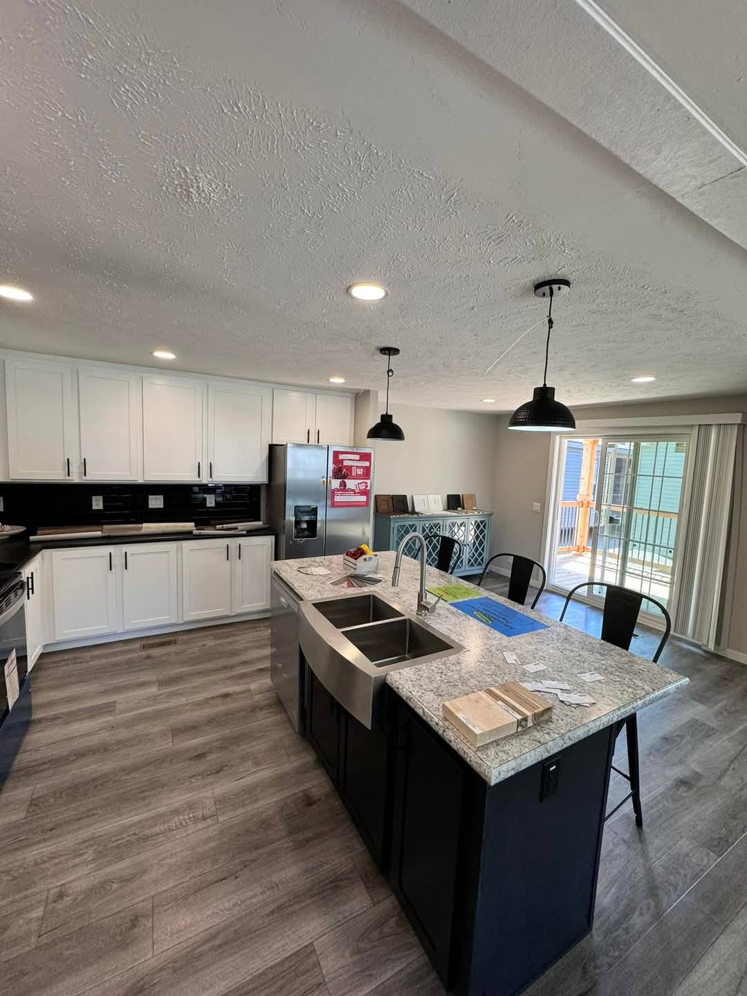 Modern kitchen with white cabinets, stainless steel appliances, and a central island with granite countertop and sink. Pendant lights and light wood floors create a bright, open feel.